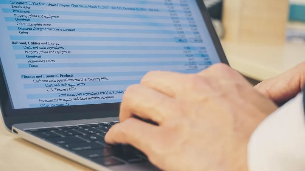A hand on a laptop trackpad, reviewing a set of financial statements on screen