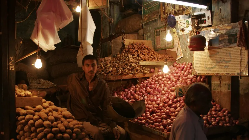 A vegetable vendor's stall stacked with onions and potatoes, lit by bare bulbs