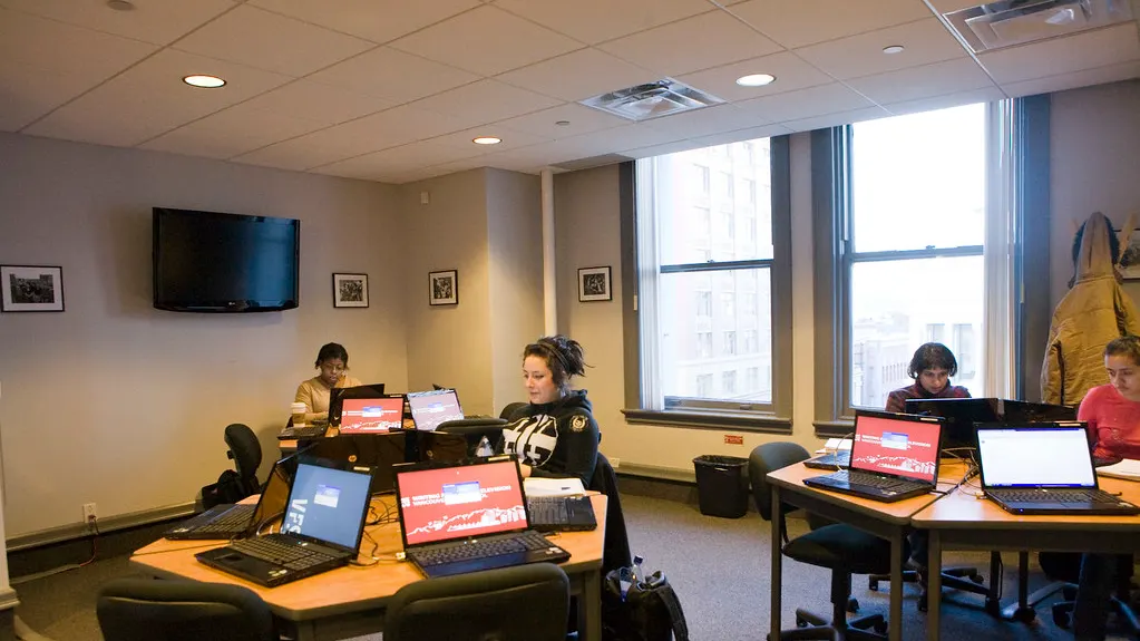 Students working at laptops around tables in a studio classroom