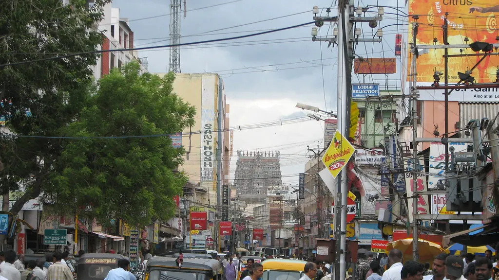 A busy street in Madurai with shops, traffic and a temple tower in the distance